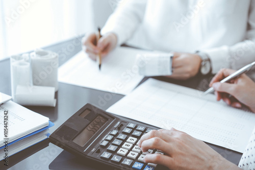 Two accountants use a calculator and laptop computer for counting taxes or revenue balance. Business, audit, and taxes concepts photo