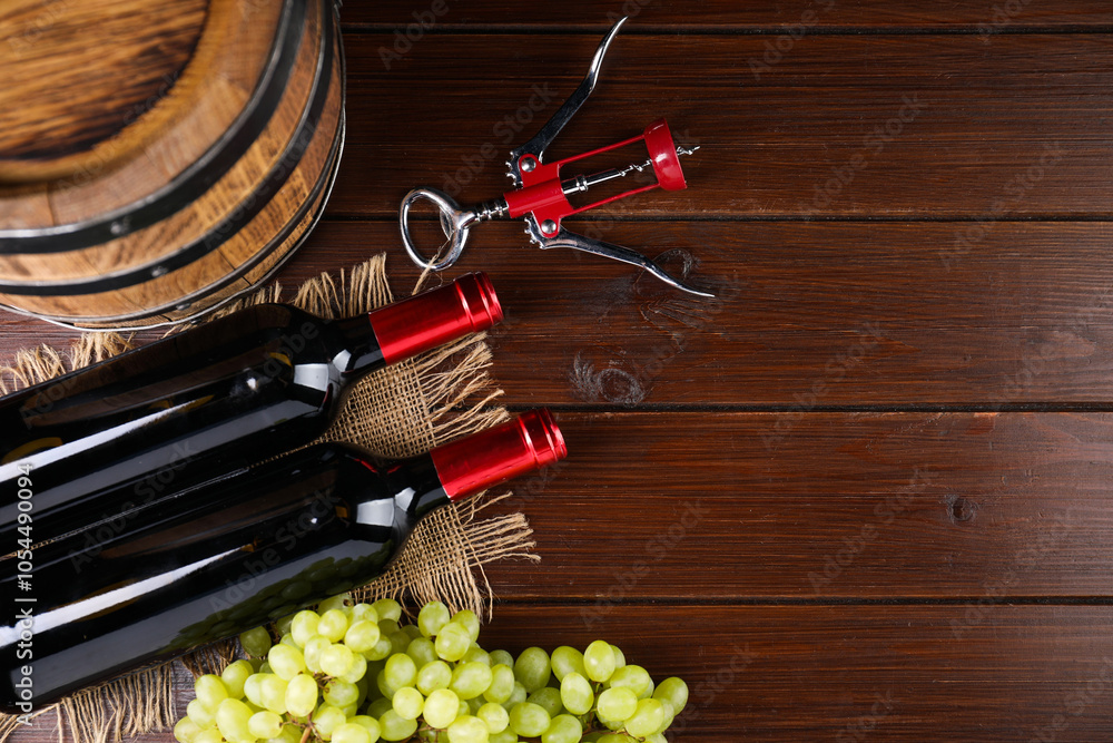 Obraz premium Wing corkscrew, bottles of wine, grapes and barrel on wooden table, top view. Space for text