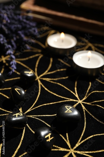 Black runes and burning candles on divination mat, closeup photo