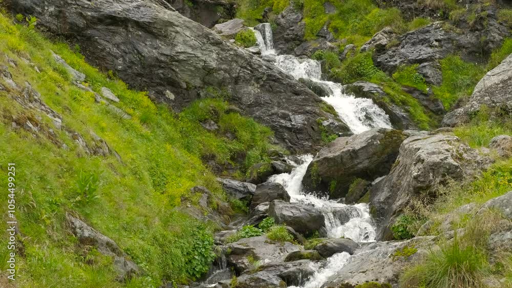 Water cascading down rocks in mountain stream. Water cascades down a rocky mountain stream, creating a soothing sound. Lush green grass lines the banks, enhancing the serene beauty of the natural Water cascading down rocks in mountain stream. Water cascades down a rocky mountain stream, creating a soothing sound. Lush green grass lines the banks, enhancing the serene beauty of the natural