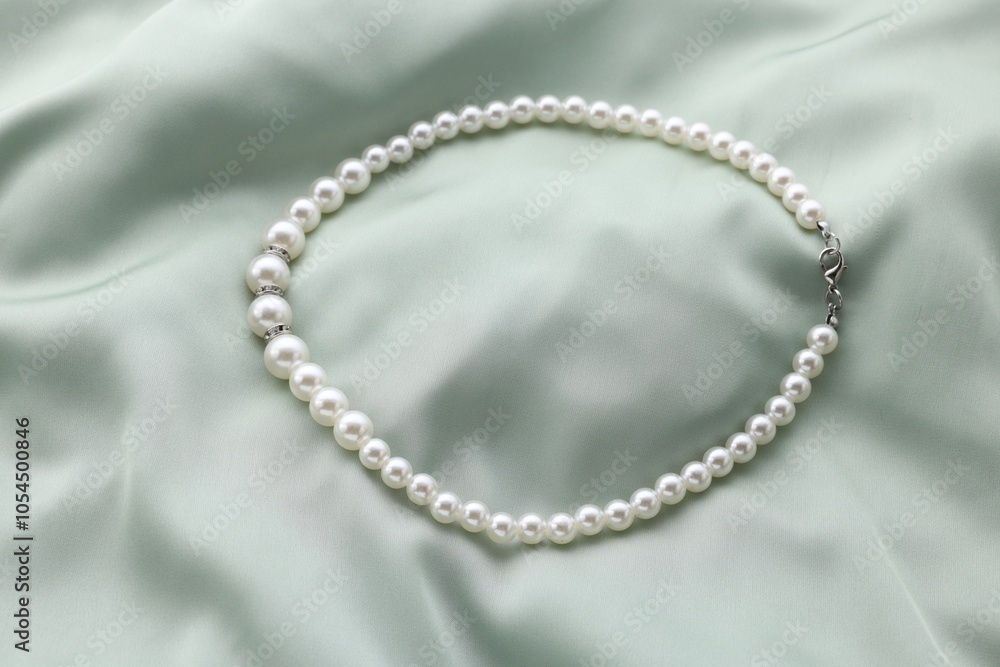 Beautiful pearl necklace on light green cloth, top view Beautiful pearl necklace on light green cloth, top view