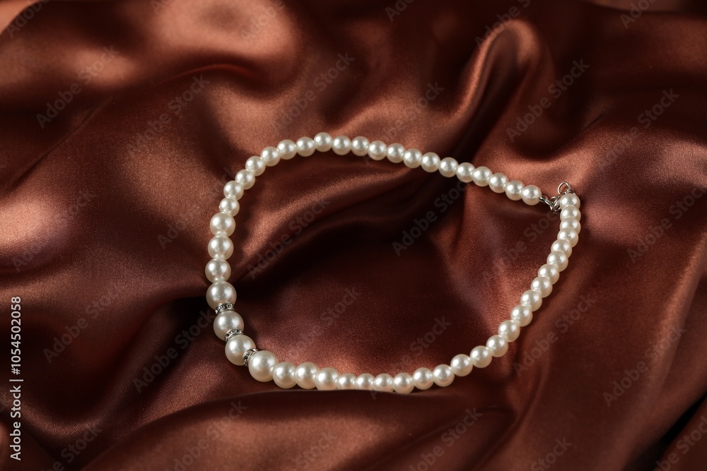 Fototapeta premium Beautiful pearl necklace on brown silky fabric