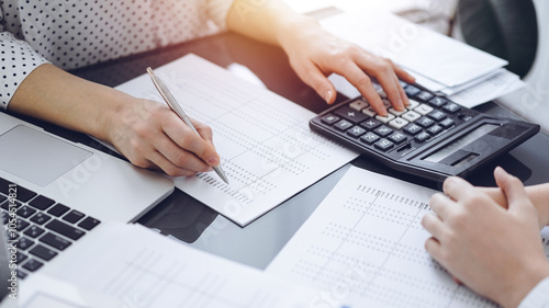 Woman accountant using a calculator and laptop computer while counting taxes with a client or a colleague. Business audit team, finance advisor