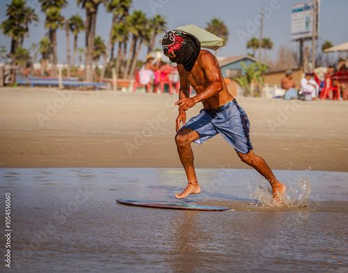 An unidentifiable skimboarder with a shirt over his head skimboarding on a beach.  photo