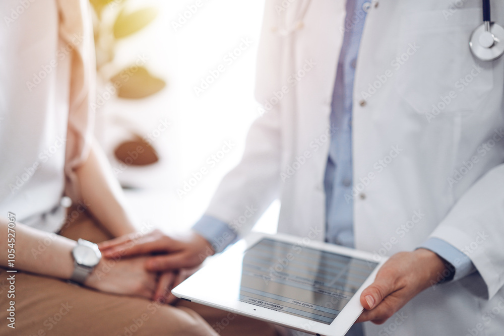 Doctor and patient discussing health exam results. Friendly physician reassuring a young woman by one hand while keeping tablet computer in another. Medicine concept Doctor and patient discussing health exam results. Friendly physician reassuring a young woman by one hand while keeping tablet computer in another. Medicine concept