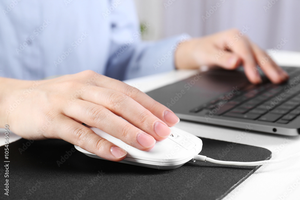 Woman using computer mouse while working with laptop at white table, closeup Woman using computer mouse while working with laptop at white table, closeup