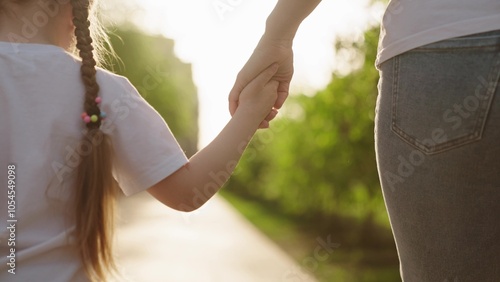 hand child close-up. child holds mother by arm park. happy family park. mom walk with kid daughter sunset. chidhood dream. sunlight healthy little child walks holding mother city park. family concept photo