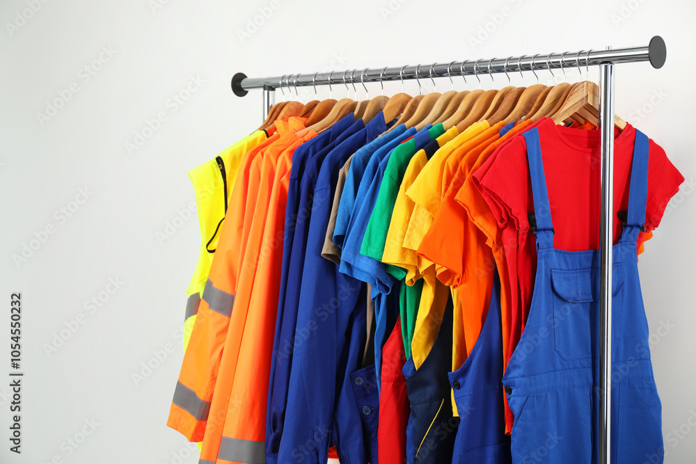Workers' uniforms on clothing rack near grey wall indoors. Space for text Workers' uniforms on clothing rack near grey wall indoors. Space for text