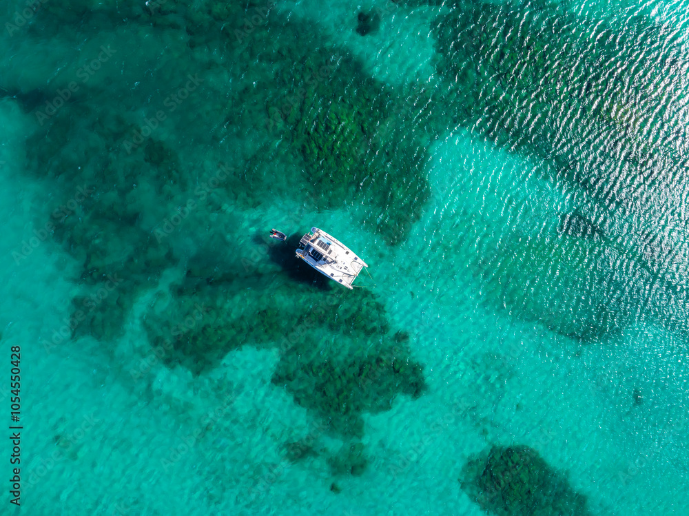A boat floats on clear turquoise waters near Sardinia, Italy, surrounded by patches of darker blue indicating deeper areas or underwater vegetation. A boat floats on clear turquoise waters near Sardinia, Italy, surrounded by patches of darker blue indicating deeper areas or underwater vegetation.