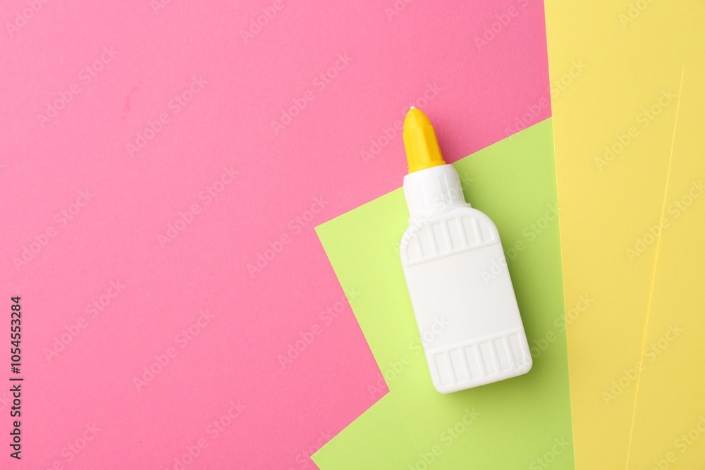 Bottle of glue and colorful paper on pink background, top view. Space for text Bottle of glue and colorful paper on pink background, top view. Space for text