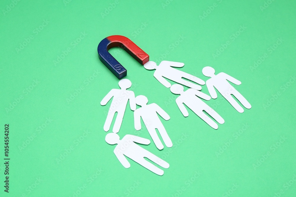 Magnet attracting paper human figures on green background Magnet attracting paper human figures on green background