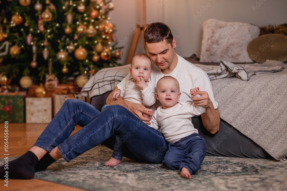 Dad with two little children is sitting near the Christmas tree Dad with two little children is sitting near the Christmas tree