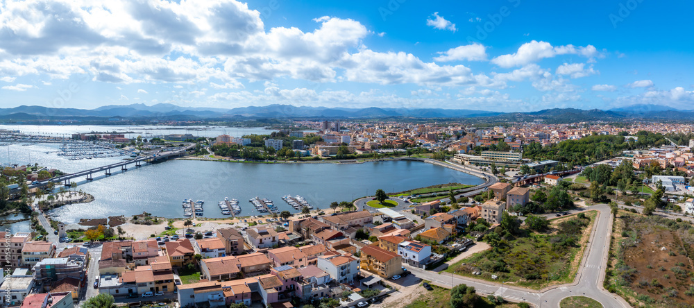 Εκτύπωση καμβά Aerial view of Olbia, Sardinia, showcasing a marina with boats, terracotta roofed buildings, a connecting bridge, and a mix of modern and traditional architecture