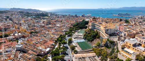 Foto Aerial view of Cagliari, Sardinia, Italy, featuring historic buildings, a sports field, and a bustling harbor with ships, set against a coastal backdrop