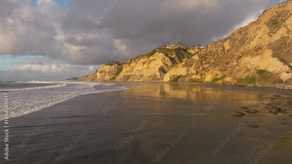 Aerial view flying along the coast of Blacks Beach in La Jolla California with views of the Pacific Ocean waves crashing along the sandy shores and the rocky cliffs during golden hour sunset Aerial view flying along the coast of Blacks Beach in La Jolla California with views of the Pacific Ocean waves crashing along the sandy shores and the rocky cliffs during golden hour sunset