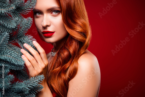 Photo of attractive lady with long ginger hait make up look touch christmas tree branch over red color background photo