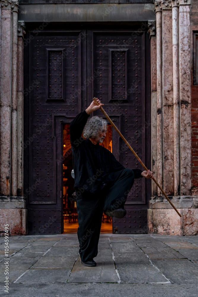 Naklejka premium middle aged tai chi master showing stick exercises outdoors amidst the architecture of a medieval cathedral