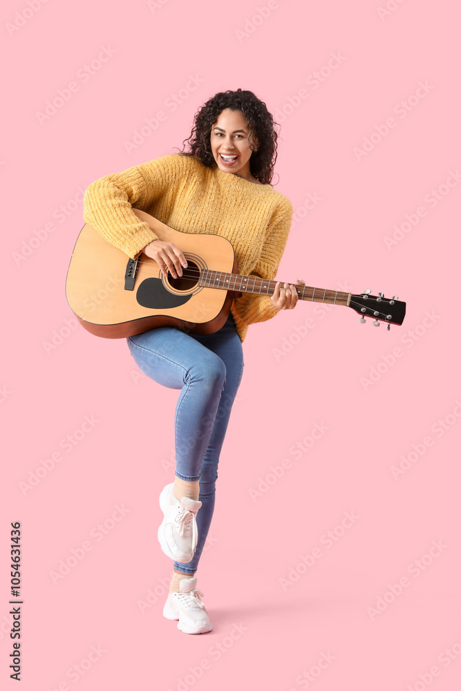 Obraz premium Young African-American woman playing acoustic guitar on pink background