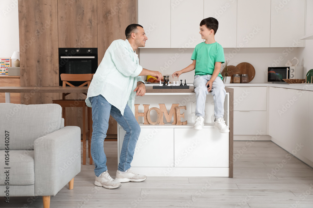 Cute little boy with his father playing chess in kitchen Cute little boy with his father playing chess in kitchen