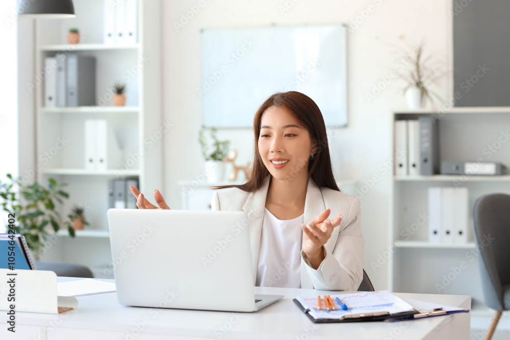 Asian businesswoman with laptop video chatting at table in office Asian businesswoman with laptop video chatting at table in office