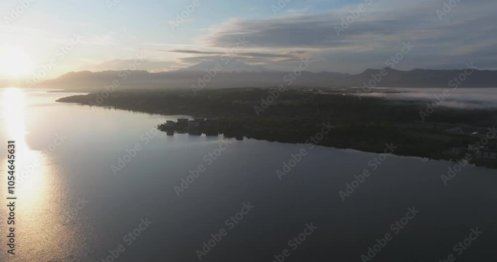 Descending aerial scene showing a residential region on the shore of the lake. Behind the imposing figure of the volcano Villarica at sunrise. Araucania, Chile Descending aerial scene showing a residential region on the shore of the lake. Behind the imposing figure of the volcano Villarica at sunrise. Araucania, Chile