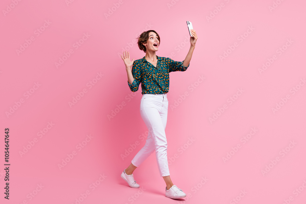 Full length photo of nice impressed woman say hi waving hand on smartphone video call go empty space isolated on pink color background Full length photo of nice impressed woman say hi waving hand on smartphone video call go empty space isolated on pink color background