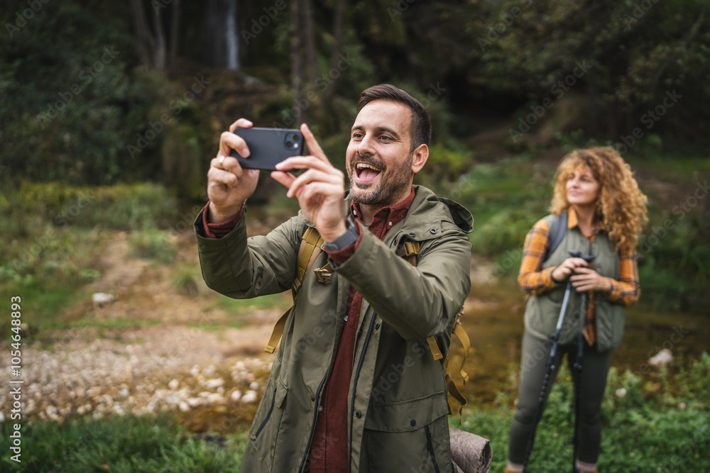 Adult man hiker take a self portrait while his wife stand behind him Adult man hiker take a self portrait while his wife stand behind him