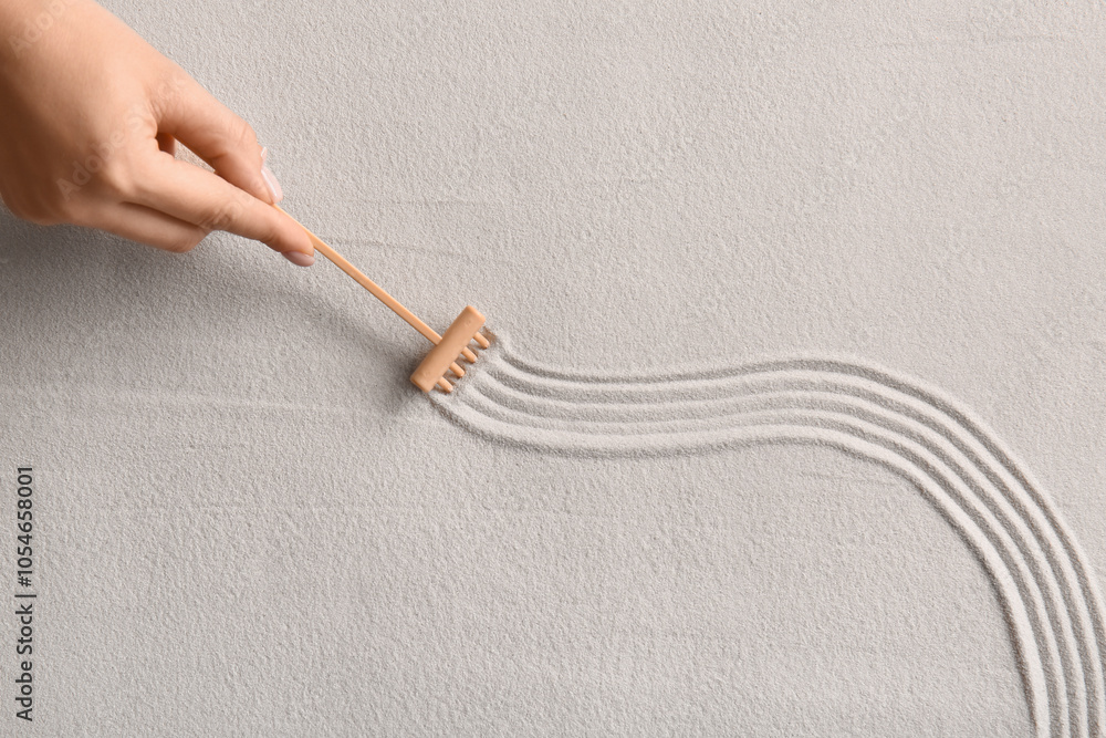 Female hand and small rake on light sand with lines. Zen concept Female hand and small rake on light sand with lines. Zen concept