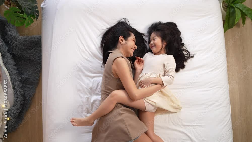 A mother and daughter lie on a bed, sharing a joyful moment with laughter and smiles. The cozy indoor setting highlights their close bond, love, and warmth, capturing a heartwarming family interaction A mother and daughter lie on a bed, sharing a joyful moment with laughter and smiles. The cozy indoor setting highlights their close bond, love, and warmth, capturing a heartwarming family interaction