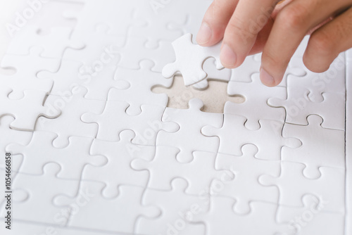 Obraz na plátne A hand is placing a missing white puzzle piece into a nearly complete puzzle on a flat surface
