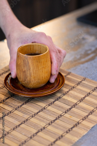 Man holding wooden cup of tea on bamboo mat, enjoying warm beverage, at home photo