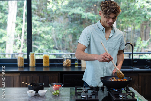 Young man cooking in modern kitchen, stirring vegetables in frying pan, at home photo