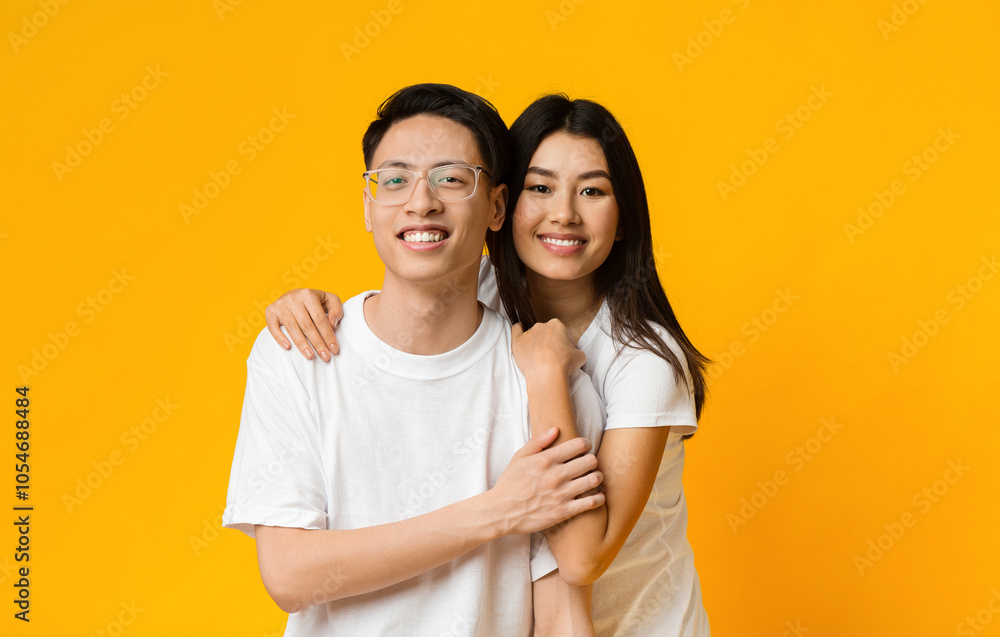Asian girl in love hugging her smiling boyfriend, yellow studio background Asian girl in love hugging her smiling boyfriend, yellow studio background