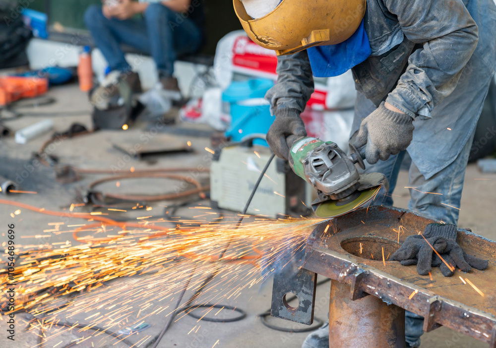 Worker grinding steel with an electric grinder. Worker grinding steel with an electric grinder.