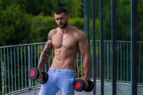 Muscular man pumps his muscles and lifts dumbbells in gym. Strong fit man exercising with dumbbells. Muscular young handsome man lifting weights. Weightlifting and training with dumbbells. photo