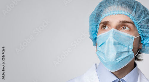 Coronavirus Fight. Confident male doctor in medical mask and hair net looking at copy space over light background, panorama