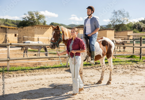 Young woman leads horse on leash with young man rider in paddock photo