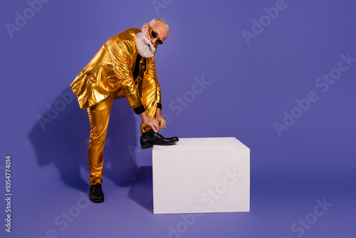 Full body photo of bearded gentleman step white cube tie shoelaces wear fashionable golden clothes isolated on violet color background