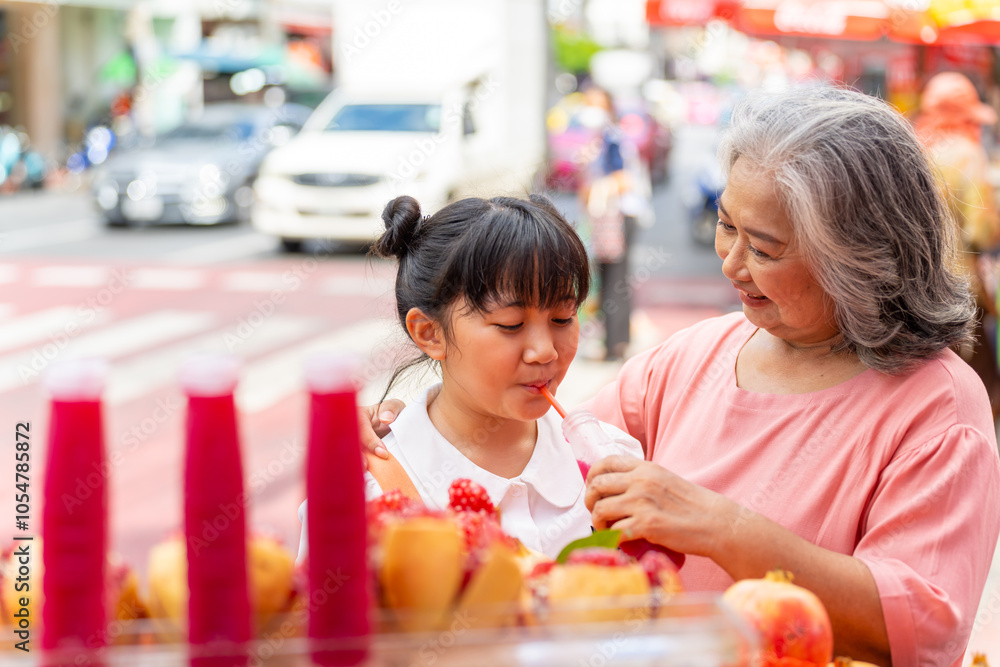 Happy Asian family grandmother and grandchild girl enjoy outdoor lifestyle shopping, eating street food and drinking pomegranate fruit juice during travel street market on summer holiday vacation. Happy Asian family grandmother and grandchild girl enjoy outdoor lifestyle shopping, eating street food and drinking pomegranate fruit juice during travel street market on summer holiday vacation.