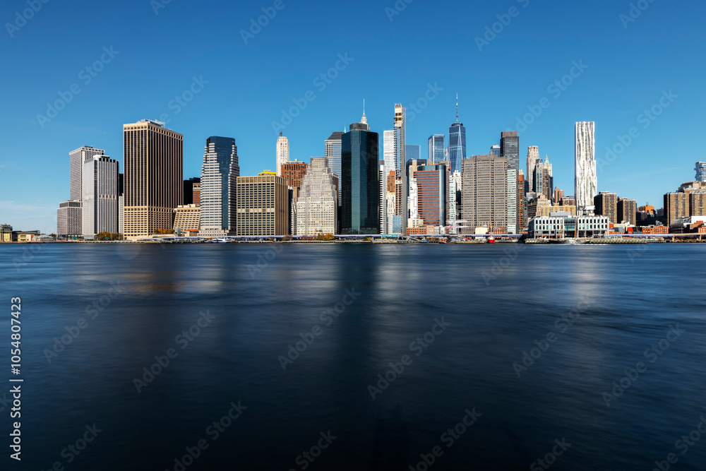 Naklejka premium Downtown Manhattan Skyline : A stunning view showcasing iconic skyscrapers and the historic bridge, beautifully illuminated at sunset, reflecting the vibrant energy of New York City