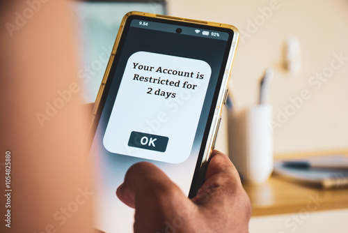 Man holding phone showing account restricted message for two days. Selective focus. Social media account restrictions concept.