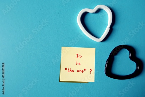 Heart shape on blue copy space background with text written IS HE THE ONE?  woman asking herself if she is falling in love the right man to commit to spend the rest of her life with. is he her soulmat