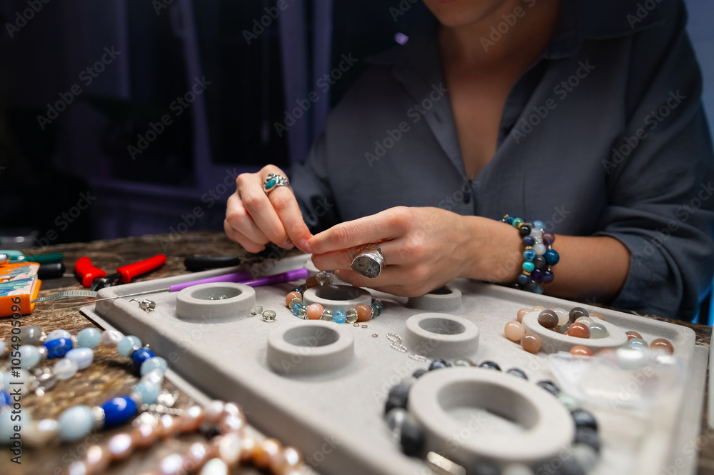 Woman assembles a bracelet of stones with her fingers and adjusts the size. Gift workshop Woman assembles a bracelet of stones with her fingers and adjusts the size. Gift workshop