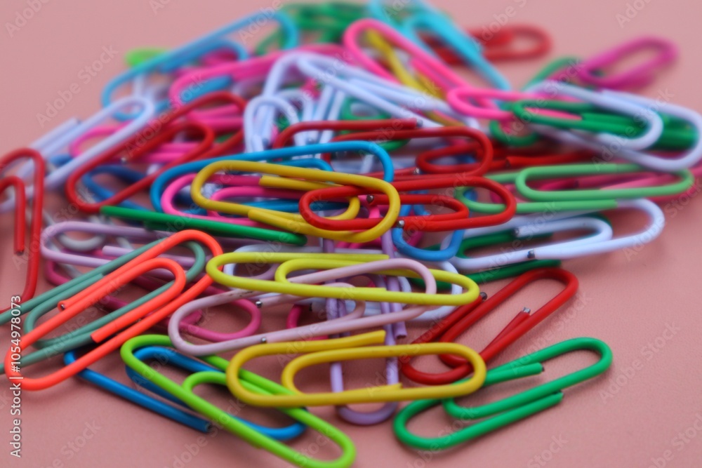 Background and texture of a Pile of colorful elliptical paper clips on a pink background, close up view. Background and texture of a Pile of colorful elliptical paper clips on a pink background, close up view.