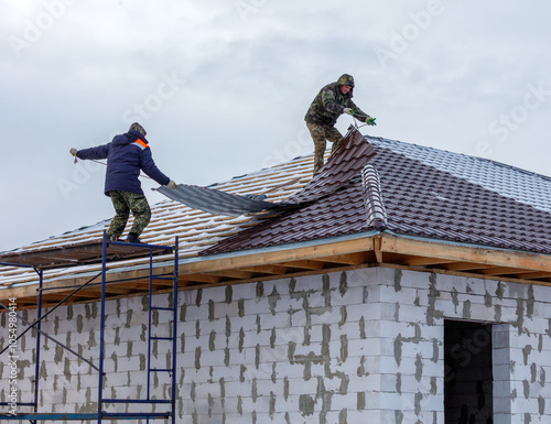 Two men are working on a roof, one of them is wearing a blue jacket