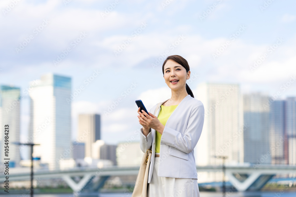 Fototapeta premium スマホ、スマートフォン、女性、ビジネスウーマン、ビジネス、キャリアウーマン、モバイル、5G、都市、通信、アプリ、屋外、青空、ブルー、社会、技術、テクノロジー、エレクトロニクス、携帯電話、ソーシャルメディア、ソーシャルネットワーク、SNS、ビル群、都会、笑顔、ユーザー、仕事、ビジネスマン、日本人、立つ、コピースペース、夕暮れ、夕焼け、タッチ、webサイト、インターネット、オンライン、メール、送信、人