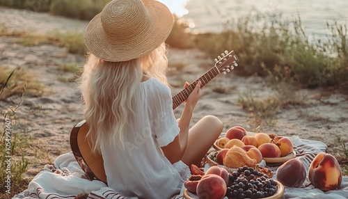 Picnic in countryside Romantic blonde woman in straw hat sitting on cover on the beach in sunset soft colors and playing ukulele guitar Fresh fruits croissants and peach on the plate photo