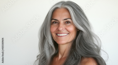 Portrait of an elegant senior woman with flowing gray hair, smiling warmly in soft, natural light, embodying timeless beauty and confidence against a simple background