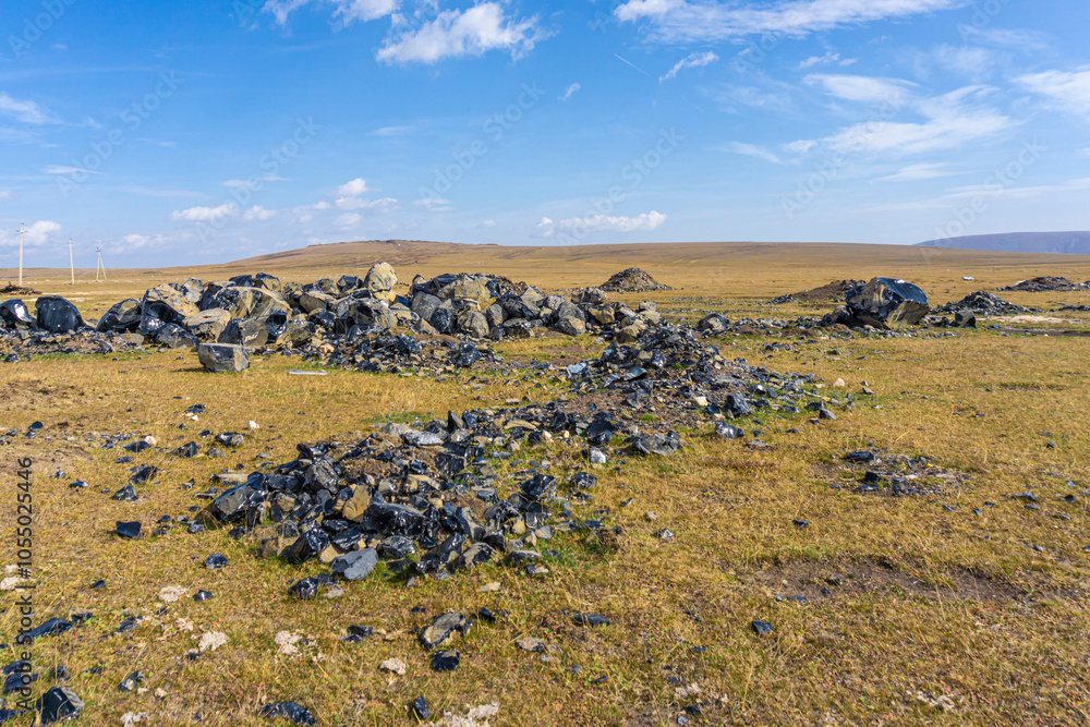 Fototapeta premium Huge obsidians lie on autumn grass in the sun. Hills and blue sky in the background