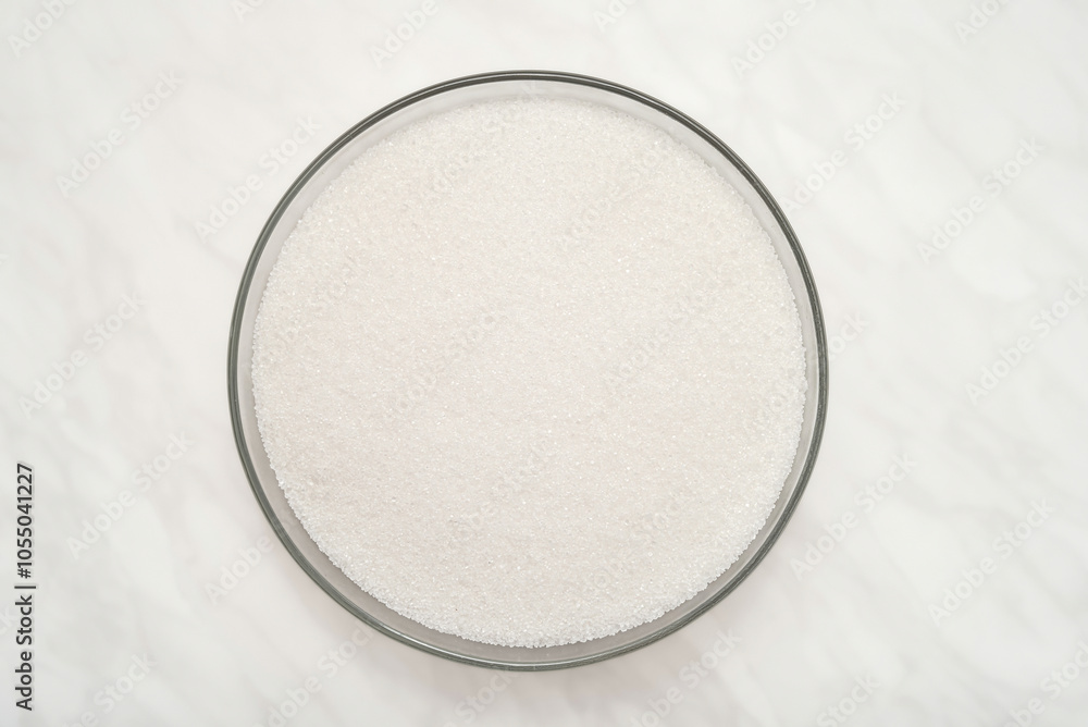 Heap of refined white sugar in the glass bowl on the light gray marble table texture. Top view. Stop diabetes and healthy diet concept. Heap of refined white sugar in the glass bowl on the light gray marble table texture. Top view. Stop diabetes and healthy diet concept.